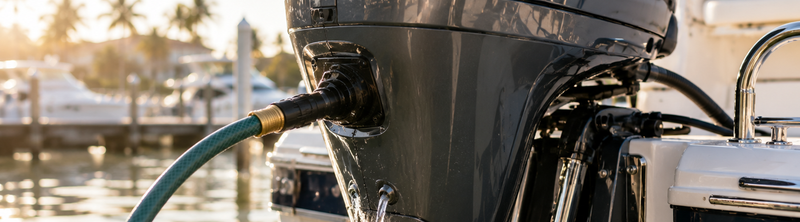 Freshwater flush hose connected to an outboard motor's earmuff fitting at a marina, used to rinse salt buildup after saltwater boating.