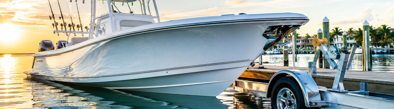 White center console fishing boat on a trailer at a marina dock during golden hour.